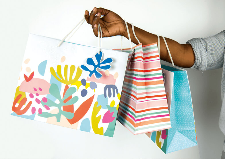 An arm holds a series of multicoloured gift bags, on a white background. 