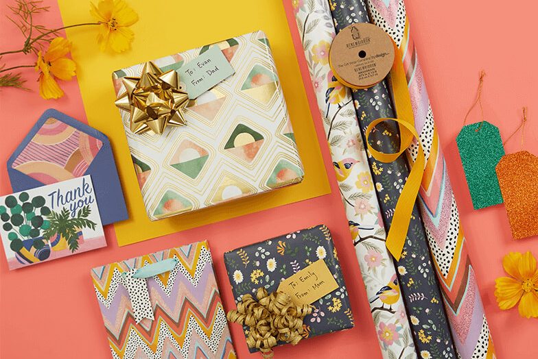 A collection of wrapped presents, rolls of gift wrap and greetings cards, laid flat on a pink and yellow background.