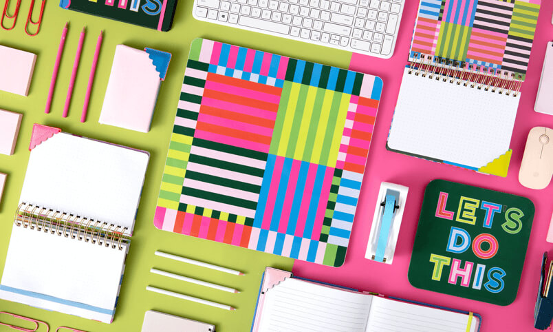 A range of create products, including notepads, books, pens and other stationery items, on a green and pink background. 