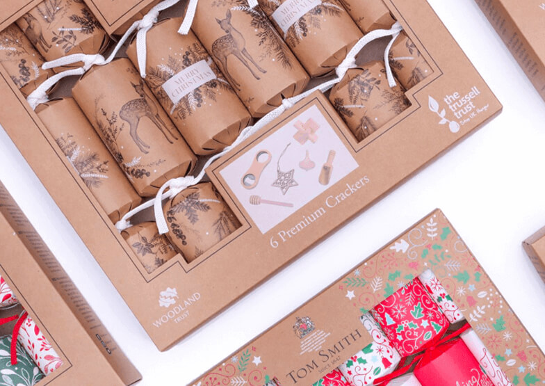 Boxes of kraft coloured Christmas Crackers laid flat on a white background. 